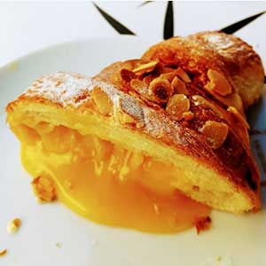 Grande plano de o melhor croissant, um croissant francês recheado com creme de leite amarelo e coberto com fatias de amêndoa torrada, num prato branco.
