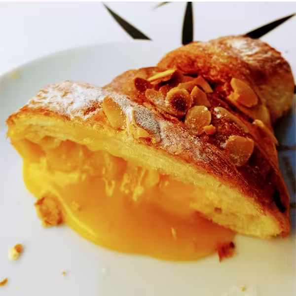 Grande plano de o melhor croissant, um croissant francês recheado com creme de leite amarelo e coberto com fatias de amêndoa torrada, num prato branco.