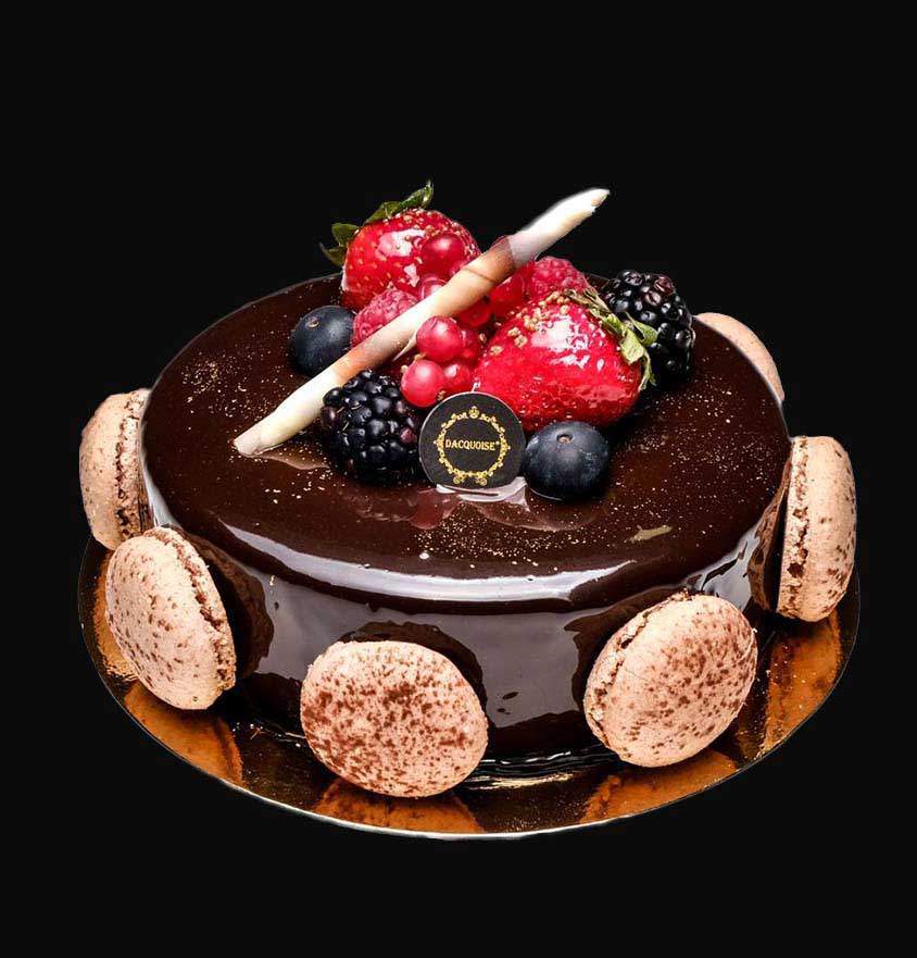 Contacto da Pâtisserie Dacquoise. Um bolo de chocolate brilhante coberto com bagas variadas, dois palitos de chocolate e uma pequena etiqueta redonda de contacto. Decorado com macarons nas laterais e com um delicado dacquoise, assenta numa base dourada sobre um fundo preto.