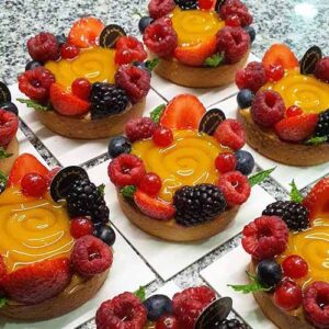 Pequenas tartes de fruta com recheio de creme amarelo brilhante, cobertas com morangos, framboesas, amoras, mirtilos, groselhas e folhas de hortelã.