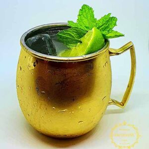 Uma caneca de metal dourada com uma bebida gelada, decorada com lima e hortelã fresca, perfeita para catering para aniversários ou qualquer catering e eventos, sobre um fundo branco liso.
