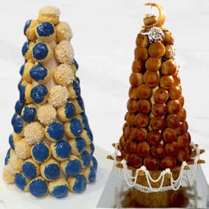 Duas torres de croquembouche altas, em forma de cone, feitas de pastéis de nata empilhados. A torre da esquerda é coberta com glacé azul e branco; a da direita é coberta com caramelo brilhante e açúcar em pó, tornando qualquer celebração em Lisboa inesquecível.