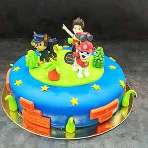Um bolo redondo decorado com fondant azul e verde, estrelas amarelas e padrões de tijolo. Apresenta topos de personagens da Patrulha Pata num cenário de relva - perfeito para adicionar à sua galeria ou partilhar como fotos dos bolos da Pâtisserie Dacquoise.