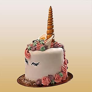 Um bolo com tema de unicórnio dos bolos da Pâtisserie Dacquoise, decorado com um corno dourado, orelhas brancas, olhos fechados com pestanas compridas e flores coloridas cor-de-rosa, roxas e verdes numa base redonda dourada - uma verdadeira galeria de doçura.