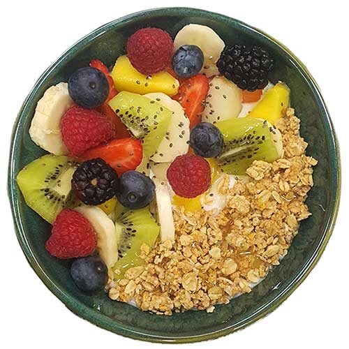Uma taça verde cheia de granola, fruta fresca e sementes de chia sobre iogurte.