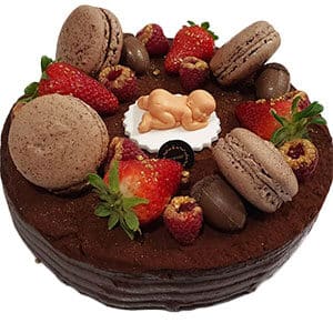 Um bolo de chocolate dos bolos da Pâtisserie Dacquoise, coberto com morangos frescos, macarons, chocolates e uma pequena estatueta de bebé comestível deitada num disco branco no centro - perfeito para a sua sobremesa galeria.