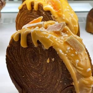 Grande plano de uma massa com camadas visíveis em espiral, coberta com uma cobertura amarela, polvilhada com açúcar grosso e decorada com pedaços de fruta cristalizada - perfeita para catering para aniversários ou catering para festas particulares.
