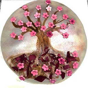 Um bolo redondo decorado com uma árvore feita de glacé castanho, coberto com muitas pequenas decorações de flores cor-de-rosa - perfeito para catering Lisboa ou catering e eventos. Pétalas e pedaços de flores cor-de-rosa estão espalhados na base da árvore.