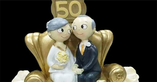 bodas de ouro. vê-se um casal muito chique sentado num sofá dourado com a imagem dos 50 anos de casados