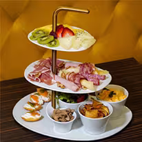 Tabuleiro para o pequeno-almoço com sumo, café, pão, fruta, carnes fatiadas, salada, pastelaria da Pâtisserie Dacquoise. O ambiente luminoso sugere uma refeição partilhada com delícias de inspiração francesa.