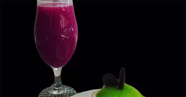 Um copo alto de sumos roxo vibrante está ao lado de um prato com uma sobremesa verde coberta com decorações de chocolate, tudo sobre um fundo preto. Perfeito para qualquer menu de bebidas que pretenda impressionar.