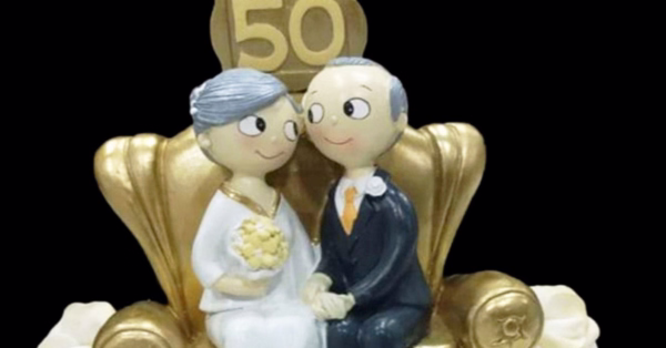 bodas de ouro. vê-se um casal muito chique sentado num sofá dourado com a imagem dos 50 anos de casados