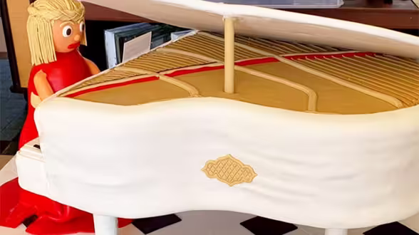 Uma mulher vestida de vermelho toca um piano de cauda branco. Bolo perfeito para um casamento