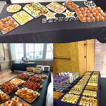 Um buffet de pequeno-almoço montado com catering ao domicílio num escritório, com pastelaria, sanduíches, fruta, copos de iogurte, sumo e copos em várias mesas