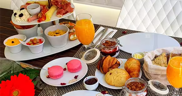 Uma exposição de tabuleiros com fatias de fruta fresca variada, incluindo kiwi, ananás, morangos e melão - perfeitos para um brunch Dacquoise vibrante em Campo de Ourique - juntamente com carnes enroladas e pequenos aperitivos em pratos brancos.