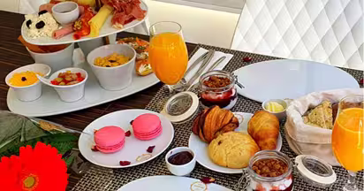 Uma exposição de tabuleiros com fatias de fruta fresca variada, incluindo kiwi, ananás, morangos e melão - perfeitos para um brunch Dacquoise vibrante em Campo de Ourique - juntamente com carnes enroladas e pequenos aperitivos em pratos brancos.