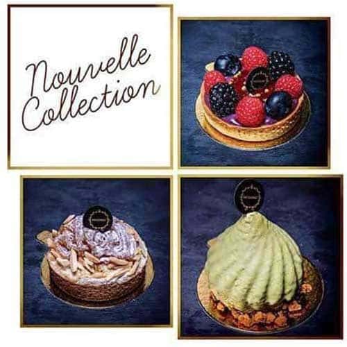 Uma seleção de pastelaria elegante e moderna das nossas Coleções Sazonais com acabamentos brilhantes e logótipos decorativos de chocolate, dispostos sobre um fundo escuro com flores brancas em primeiro plano.