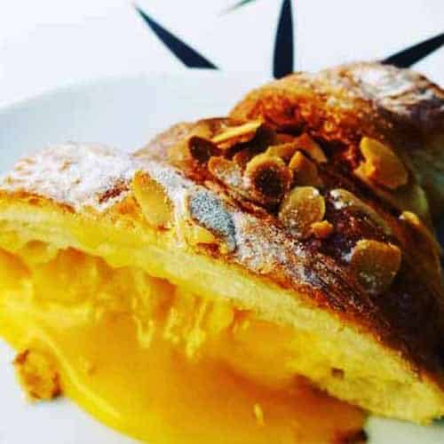 Grande plano de o melhor croissant, um croissant francês recheado com creme de leite amarelo e coberto com fatias de amêndoa torrada, num prato branco.