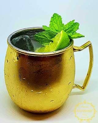 Uma caneca de metal dourada com uma bebida gelada, decorada com lima e hortelã fresca, perfeita para catering para aniversários ou qualquer catering e eventos, sobre um fundo branco liso.