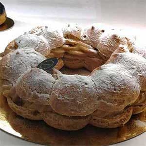 Um bolo Paris Brest em forma de anel, coberto com açúcar em pó e recheado com um creme de nozes, assenta numa tábua dourada sob uma luz suave - uma delícia clássica do bolo Paris Brest.