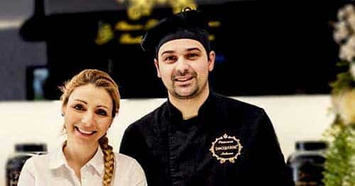 Uma mulher sorridente e o Chefe Ivo Camões estão atrás de um balcão de pastelaria. Um letreiro preto e dourado de uma pastelaria é visível ao fundo, dando um vislumbre de quem somos.